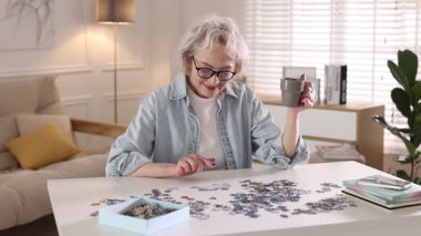 Beyaz masadaki yapbozu çözen bir bardak içkili kadın.