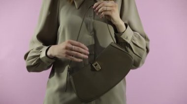 Poşetten bir şişe kozmetik ürünü alan ve pembe arka planda parfüm sıkan bir kadın.