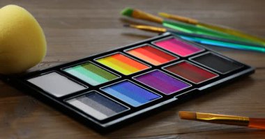 Ahşap masada yüz boyama için fırça ve palet kullanan kadın.