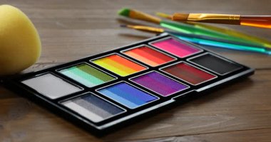 Ahşap masada yüz boyama için fırça ve palet kullanan kadın.