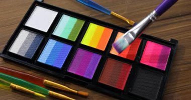 Ahşap masadaki yüz boyama için fırça ve palet kullanın.