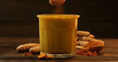 Ahşap masadan bir bardak nefis zerdeçal latte alan kadın, pudra ekledikten sonra, yakın plan.