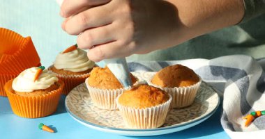Mavi masada nefis havuçlu keklerin üzerine krem şanti sıkan bir kadın.