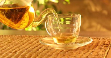 Taze demlenmiş çayı cam fincana dökerek ve çaydanlığı masaya koyarak.