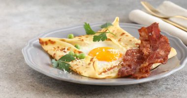 Gri masada yumurta ve pastırmalı leziz krepe parmesan peyniri ekleyen kadın, yakın plan. Breton galeti