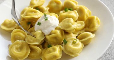 Gri desenli masada çatalla ekşi kremaya lezzetli hamur tatlısı batırmak. Yakın plan.