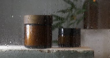 Taş yüzeyindeki kavanozlarda vücut bakımı ürünleri, damlayan damlalarla ıslak camların içinden bakmak.