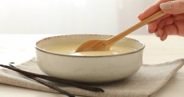 Loş masada konsantre vanilyalı sütü karıştıran kadın, yakın plan.