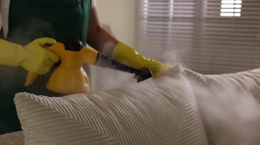 Profesyonel temizlikçi koltuğunu evde buharlı temizleyici ile temizliyor.