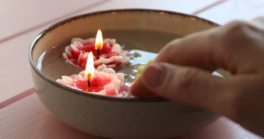 Kadın ve güzel yanan çiçek tabakta mumlar pembe ahşap masada suyla, yakın plan.