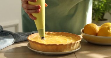 Ahşap masada çırpılmış yumurta beyazını limonlu pastaya sıkıştıran kadın, yakın plan. Kremalı tatlı yapıyorum.