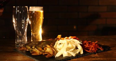 Kadın bardağa bira dolduruyor ve ahşap masada farklı kurutulmuş balık atıştırmalıkları, yakın plan