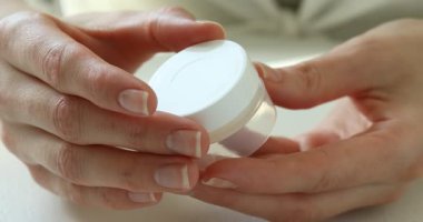 Beyaz masadaki kadın açılıp nemlendirici dudak kremi kullanıyor.