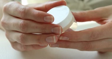 Beyaz masadaki kadın açılıp nemlendirici dudak kremi kullanıyor.