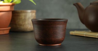 Ahşap masada çaydanlıktan fincana aromatik çay dökülüyor. Gri arka plan, yakın plan.