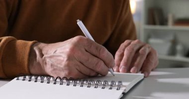 Üst düzey bir adam çevrimiçi olarak masa başında çalışırken notlar alıyor, yakın plan. Kendi kendine çalışma.