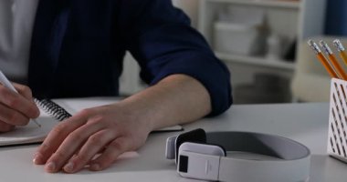 Kendi kendine çalışma. İçerideki masada ders sırasında not alan bir adam, yakın plan. Kamera sola hareket ediyor