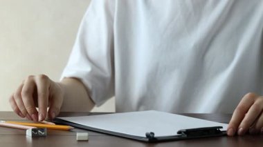 Ahşap masadaki kağıdın üzerine grafit kalemle yazan kadın, yakın plan.