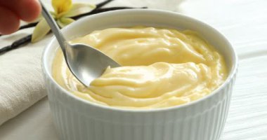 Beyaz ahşap masada nefis vanilyalı puding yiyen bir kadın.