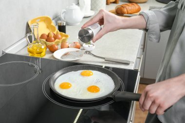 Mutfakta fırında yumurta pişirirken tavaya tuz ekleyen kadın, yakın plan.