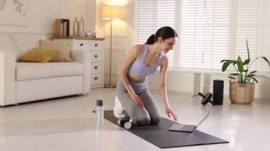 Kadın evde dizüstü bilgisayarla video dersi izlerken dambıllarla egzersiz yapıyor.