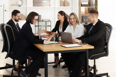 Ofisteki ahşap masada farklı aletlerle çalışan iş arkadaşları.