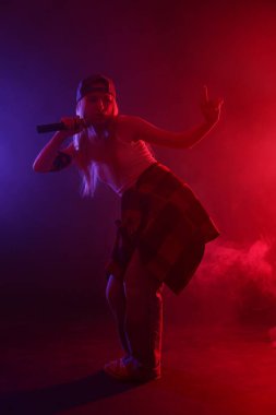 Esmer arka planda, renkli ışıklar ve dumanla şarkı söyleyen yetenekli bir şarkıcı.