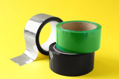 Sarı arka planda farklı yapışkan bantların ruloları, yakın plan.