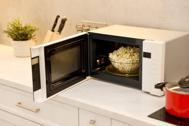 Mikrodalga fırını aç, mutfakta beyaz mermer tezgahta patlamış mısır kasesi var.