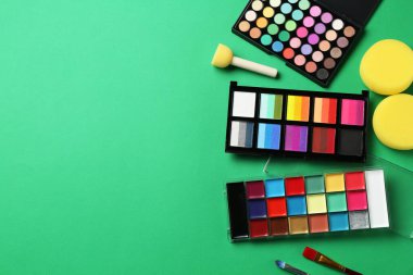 Yeşil arka planda yüz boyaları, aletler ve makyaj malzemeleri, düz yatak. Metin için boşluk