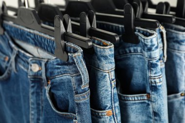 Many stylish jeans with hangers, closeup view
