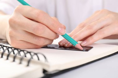 Beyaz masadaki deftere cetvel ve kalemle çizim yapan kadın, yakın plan.