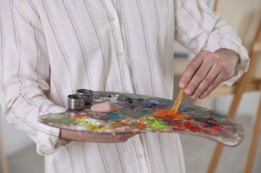 Sanatçının stüdyosunda boyaları palette karıştıran adam, yakın plan.