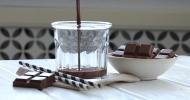 Beyaz tahta masada çikolatalı sütü bardağa dolduran kadın, yakın plan.