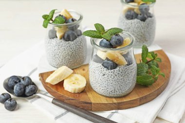 Yaban mersinli lezzetli chia pudingi, muzlu ve naneli bardaklar ışıklı masada, yakın plan.