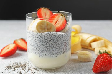 Çilekli lezzetli chia pudingi ve açık gri masada muz, yakın plan.