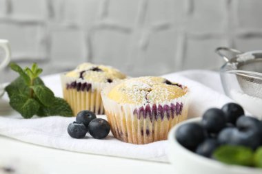 Yaban mersinli lezzetli çörekler, pudra şekeri ve nane şekeri beyaz masa üzerinde gri desenli arka plan, yakın plan