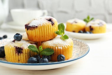 Yaban mersinli lezzetli kekler, pudra şekeri ve beyaz ahşap masada nane şekeri, yakın plan.