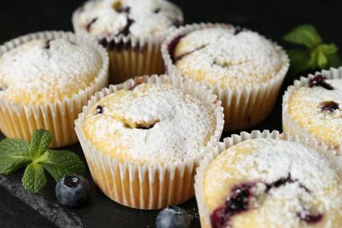 Yaban mersinli lezzetli çörekler, pudra şekeri ve nane şekeri siyah masada, yakın plan.