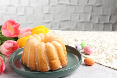 Lezzetli kek, paskalya yumurtaları ve laleler gri masada, yakın plan.