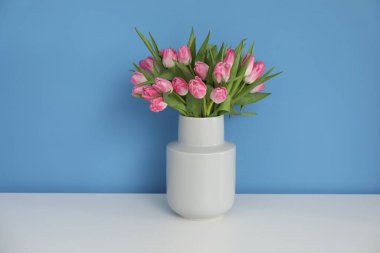 Vazodaki güzel laleler beyaz masada açık mavi arka planda.