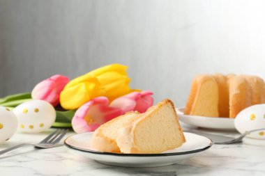 Lezzetli kek parçaları, Paskalya yumurtaları ve laleler açık mermer masada.