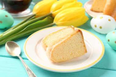 Lezzetli kek parçaları, Paskalya yumurtaları, laleler ve çay açık mavi ahşap masada, yakın plan.