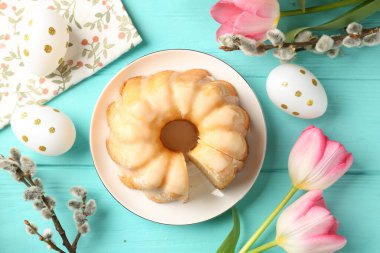 Lezzetli bohça keki, Paskalya yumurtaları, söğüt dalları ve açık mavi ahşap masa üzerindeki laleler.