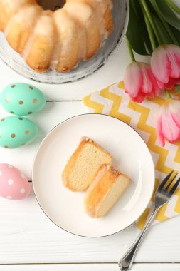 Lezzetli kek parçaları, beyaz ahşap masada paskalya yumurtası ve laleler.
