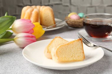 Lezzetli kek parçaları, Paskalya yumurtaları, laleler ve çay gri masada, yakın plan.