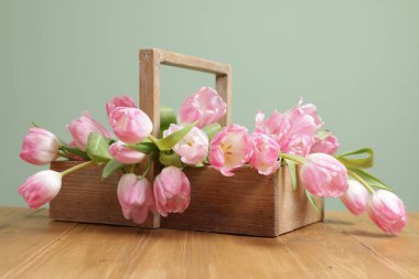 Güzel laleler sepetin içinde ahşap masada açık yeşil arka planda, yakın plan
