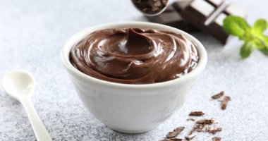 Çikolata parçacıklarını kaşıktan kaseye koyup açık gri desenli masaya lezzetli pudingler koyuyorlar. Yakın plan.