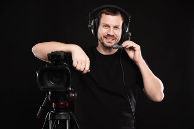 Profesyonel kameralı ve kulaklıklı bir adam siyah arka planda.