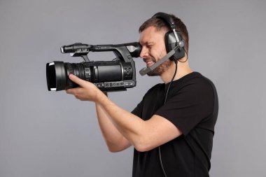 Profesyonel kameralı ve kulaklıklı bir adam gri arka planda.